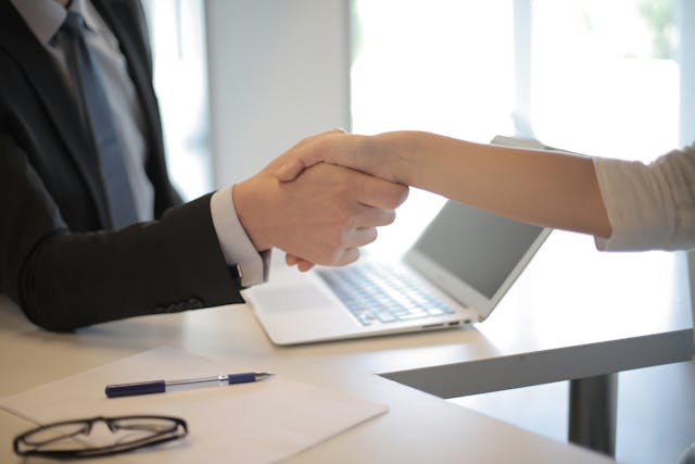 Two-people-shaking-hands-over-a-laptop