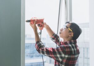 maintenance working in plaid shirt using electric drill on a window frame