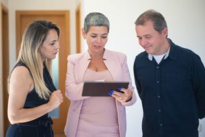 landlord in a pink suit showing two tenants something on an iPad